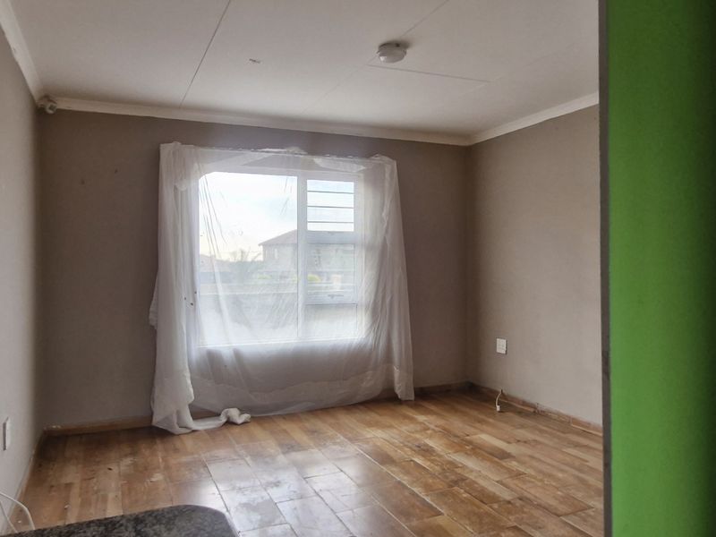 An empty bedroom featuring laminate flooring, a sliding window, and neutral wall finishes, offering a blank canvas for potential updates.