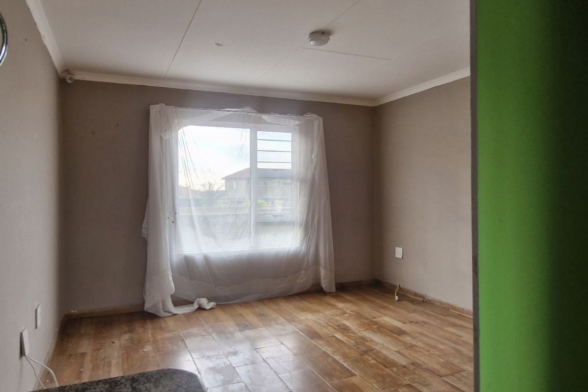 An empty bedroom featuring laminate flooring, a sliding window, and neutral wall finishes, offering a blank canvas for potential updates.