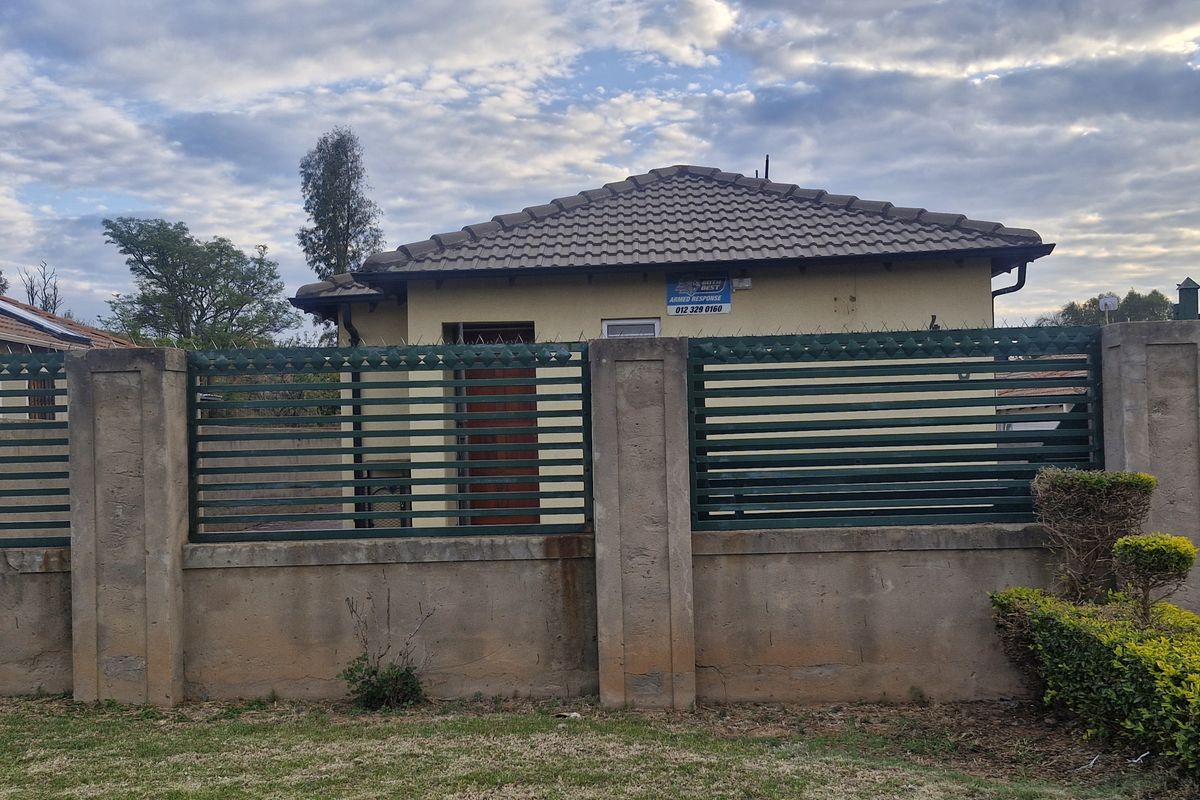 Front view of a residential property featuring a concrete boundary wall with metal security fencing, tiled roof, and an installed solar water heater.