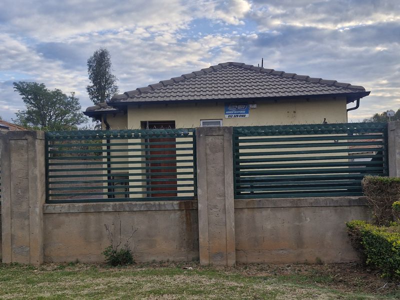 Front view of a residential property featuring a concrete boundary wall with metal security fencing, tiled roof, and an installed solar water heater.