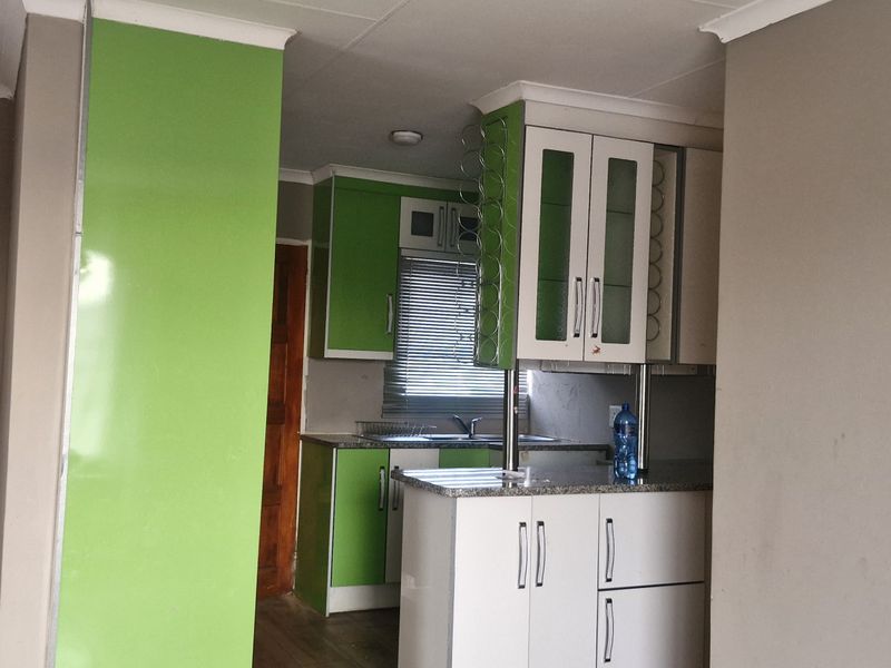 A compact kitchen featuring bright green and white cabinetry, laminate countertops, and a stainless steel sink, offering a functional layout for modern updates.