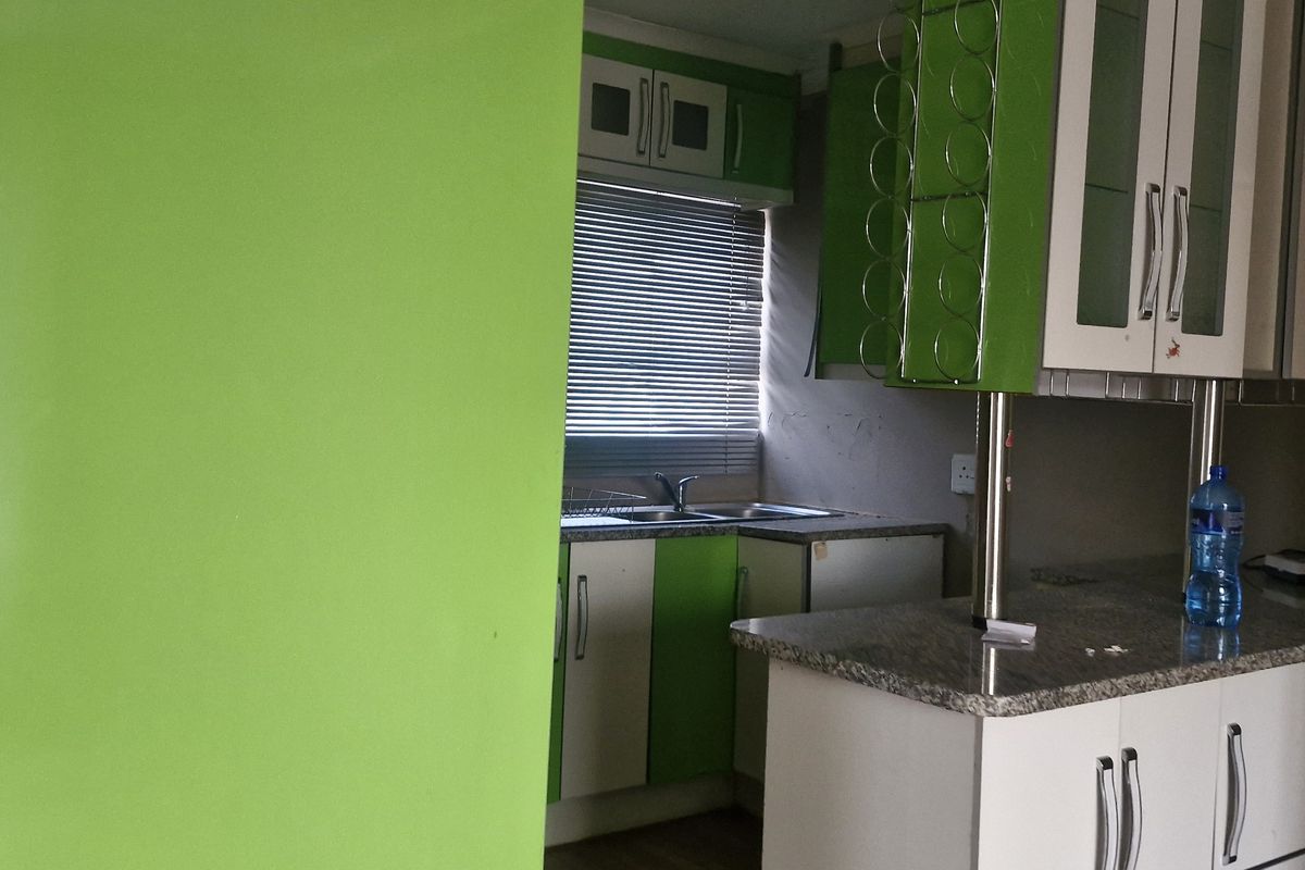 A compact kitchen featuring granite countertops, built-in cabinetry with a vibrant green finish, and a double sink with window views.