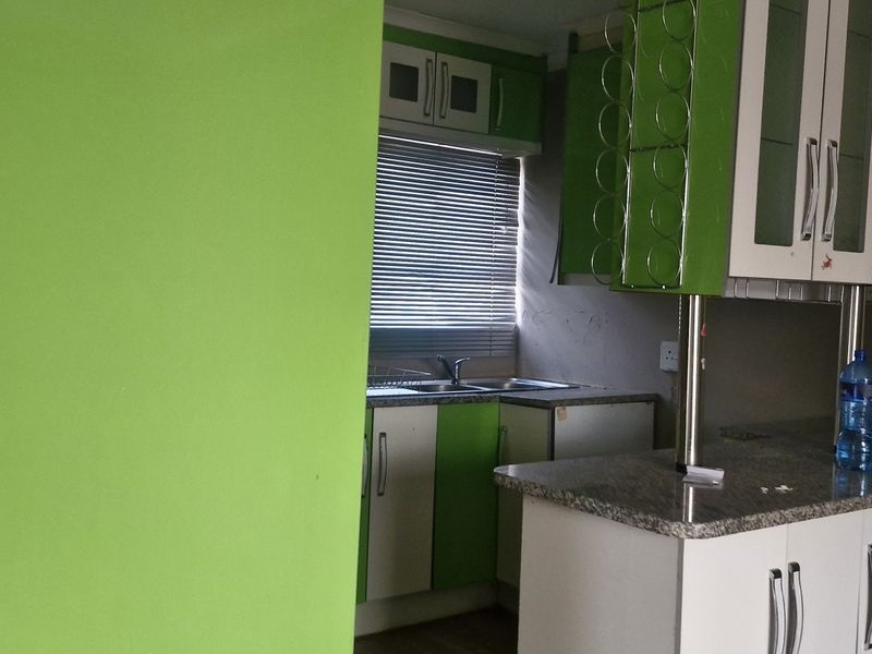 A compact kitchen featuring granite countertops, built-in cabinetry with a vibrant green finish, and a double sink with window views.