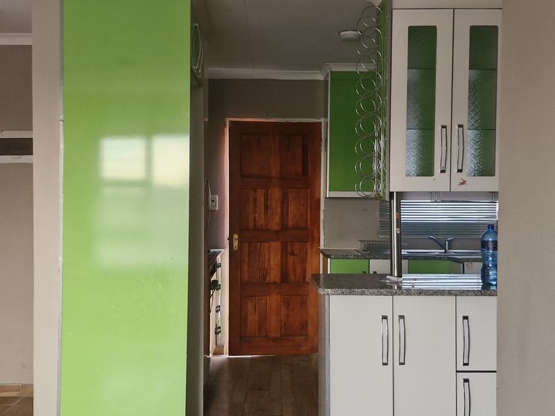 A functional kitchen area featuring fitted cabinetry, granite countertops, and a stainless steel sink, with direct access to adjacent rooms via wooden doors.