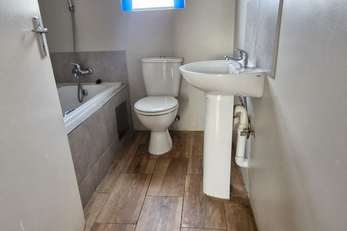 A functional bathroom featuring a pedestal basin, toilet, and a built-in bathtub with tiled finishes and wood-look flooring.