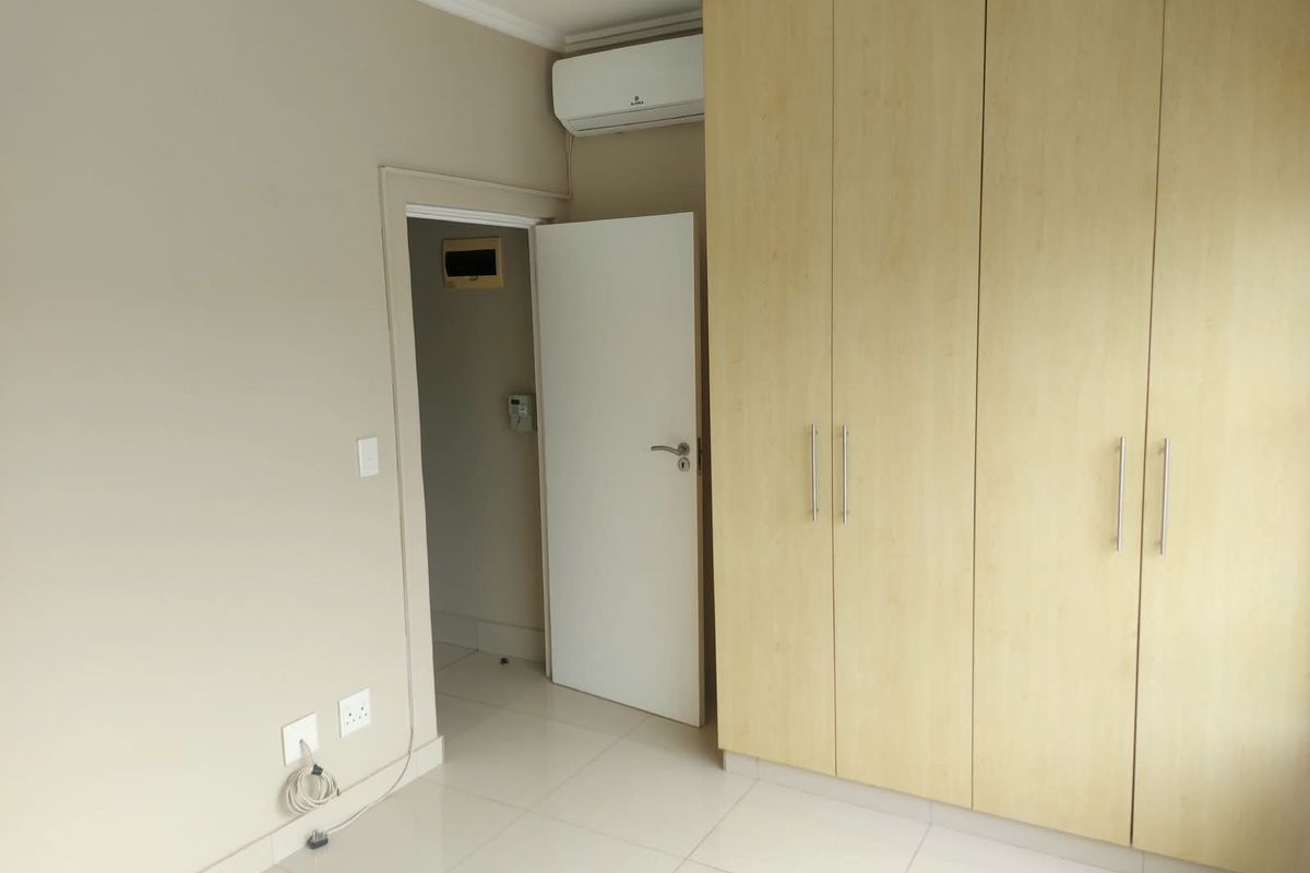 A clean, empty bedroom featuring light-toned built-in cupboards, tiled flooring, and a wall-mounted air conditioning unit.