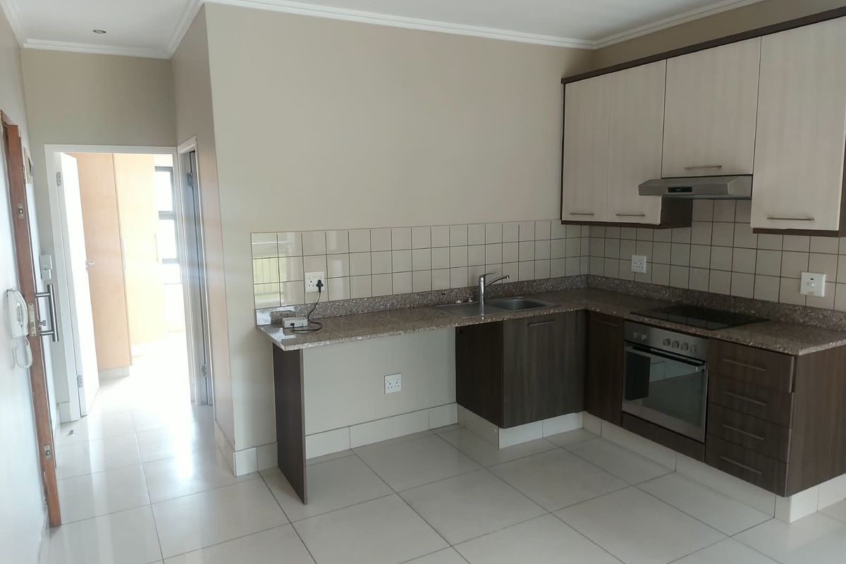A clean, functional kitchen featuring two-tone cabinetry, granite countertops, integrated oven and hob, and neutral tiled flooring.