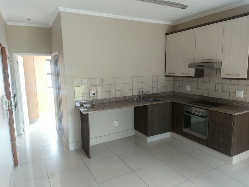A clean, functional kitchen featuring two-tone cabinetry, granite countertops, integrated oven and hob, and neutral tiled flooring.