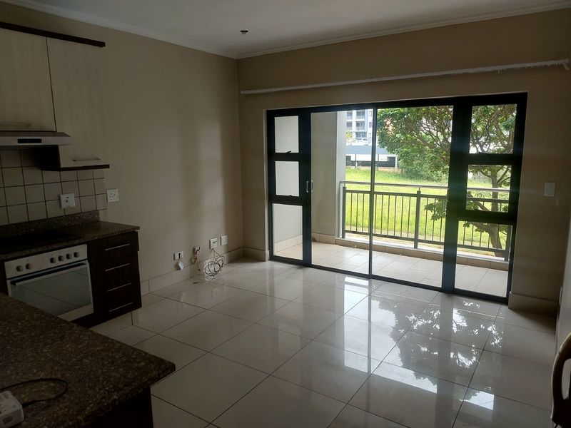 Open-plan living area featuring tiled floors, a modern kitchen with granite countertops and built-in appliances, leading to a private balcony with outdoor views.