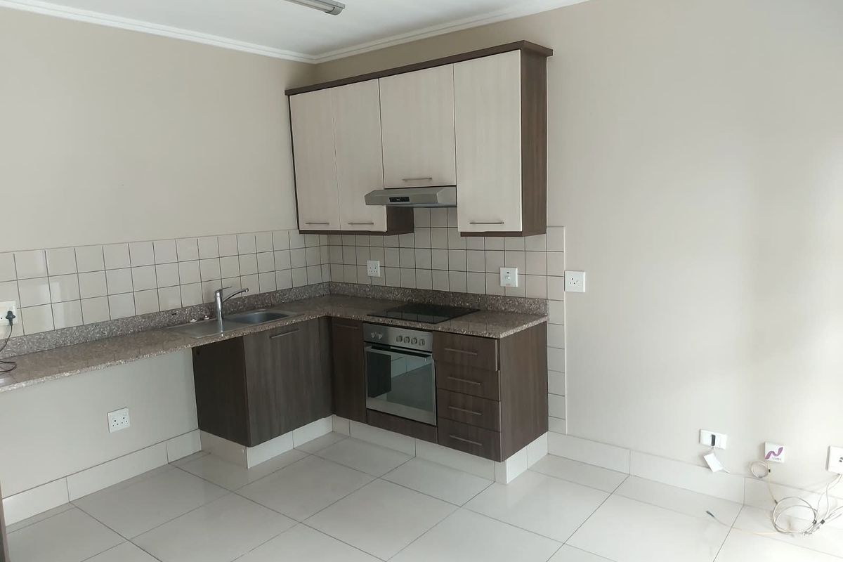 A clean, modern kitchen featuring built-in cabinetry, stone countertops, a stainless steel sink, and integrated oven and hob with a tiled backsplash.
