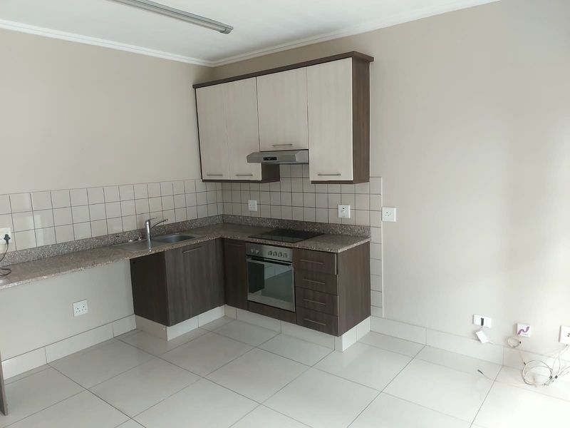 A clean, modern kitchen featuring built-in cabinetry, stone countertops, a stainless steel sink, and integrated oven and hob with a tiled backsplash.