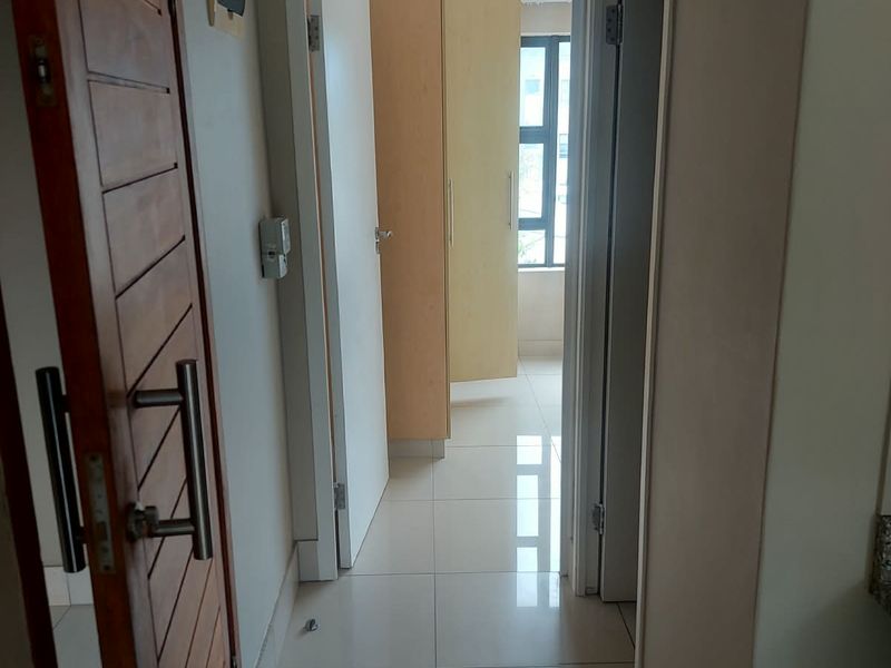 A clean, tiled hallway leading to a bedroom area featuring built-in cupboards and modern wooden door finishes.