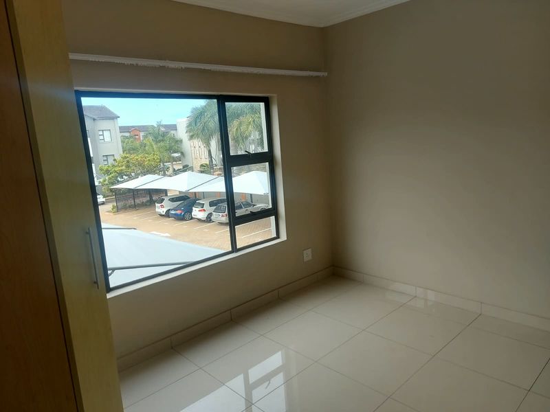 An empty bedroom featuring tiled flooring, a built-in cupboard, and a large window with views over the complex parking area.