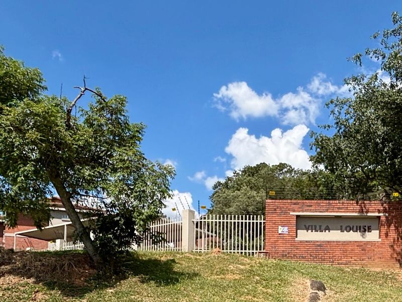 The entrance to Villa Louise complex featuring a brick boundary wall, secure metal gate, and integrated electric fencing.