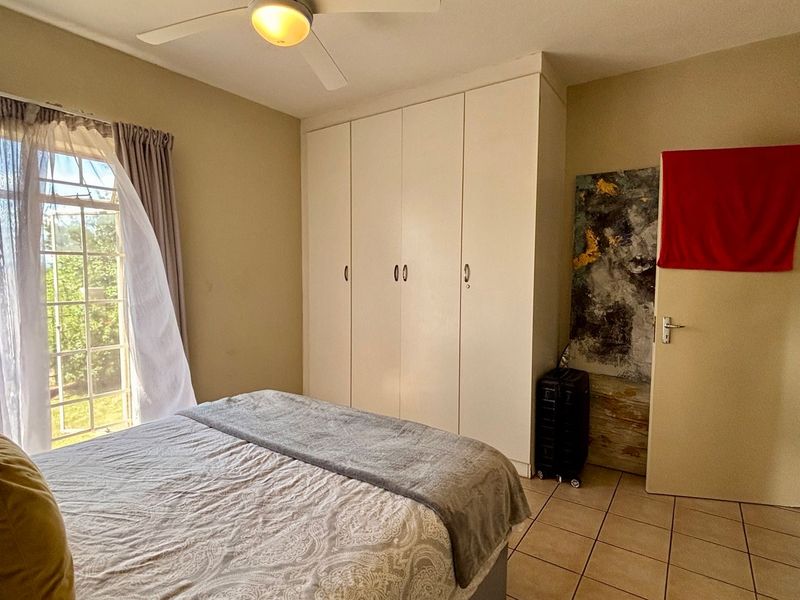 A bedroom featuring built-in cupboards, tiled flooring, and a ceiling fan, with natural light provided by a large window.