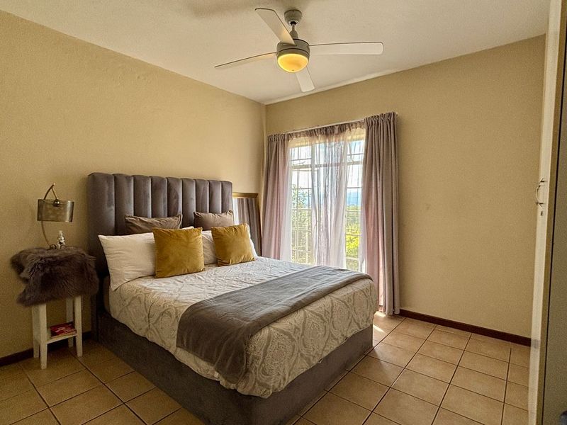 A comfortable bedroom featuring tiled flooring, a ceiling fan, and a built-in cupboard, with natural light entering through the window.