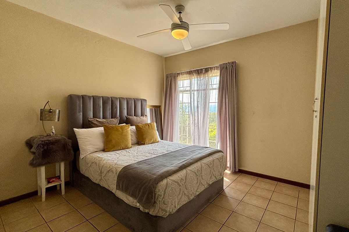 A comfortable bedroom featuring tiled flooring, a ceiling fan, and a built-in cupboard, with natural light entering through the window.