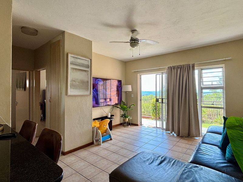 A living room featuring tiled flooring, a ceiling fan, and a sliding glass door that opens to an outdoor area with views.