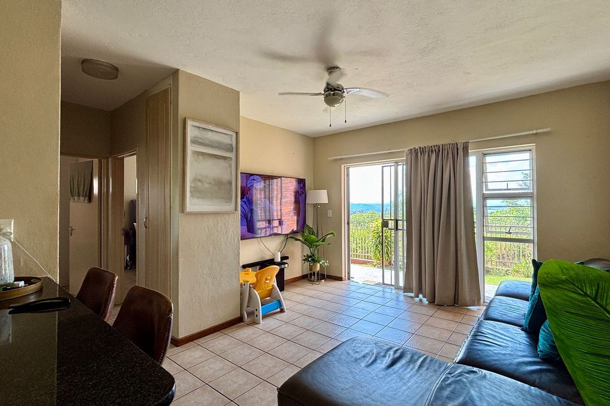 A living room featuring tiled flooring, a ceiling fan, and a sliding glass door that opens to an outdoor area with views.