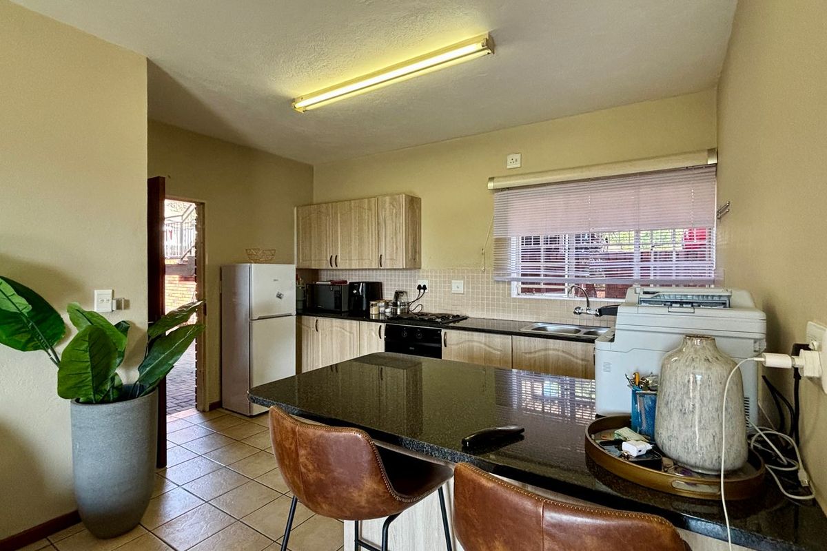 Functional kitchen featuring wood-finish cabinetry, granite countertops, built-in oven and hob, and tiled flooring with a breakfast bar area.