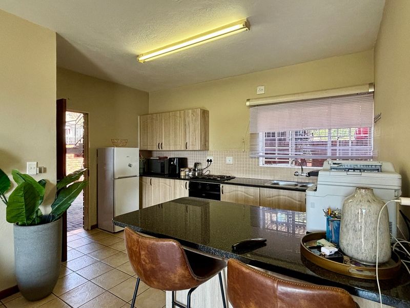 Functional kitchen featuring wood-finish cabinetry, granite countertops, built-in oven and hob, and tiled flooring with a breakfast bar area.