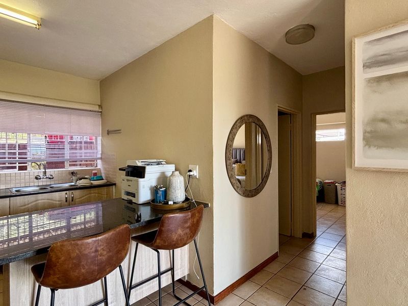 Open plan kitchen area featuring granite countertops, double sink, and tiled flooring, leading into a hallway with access to additional rooms.