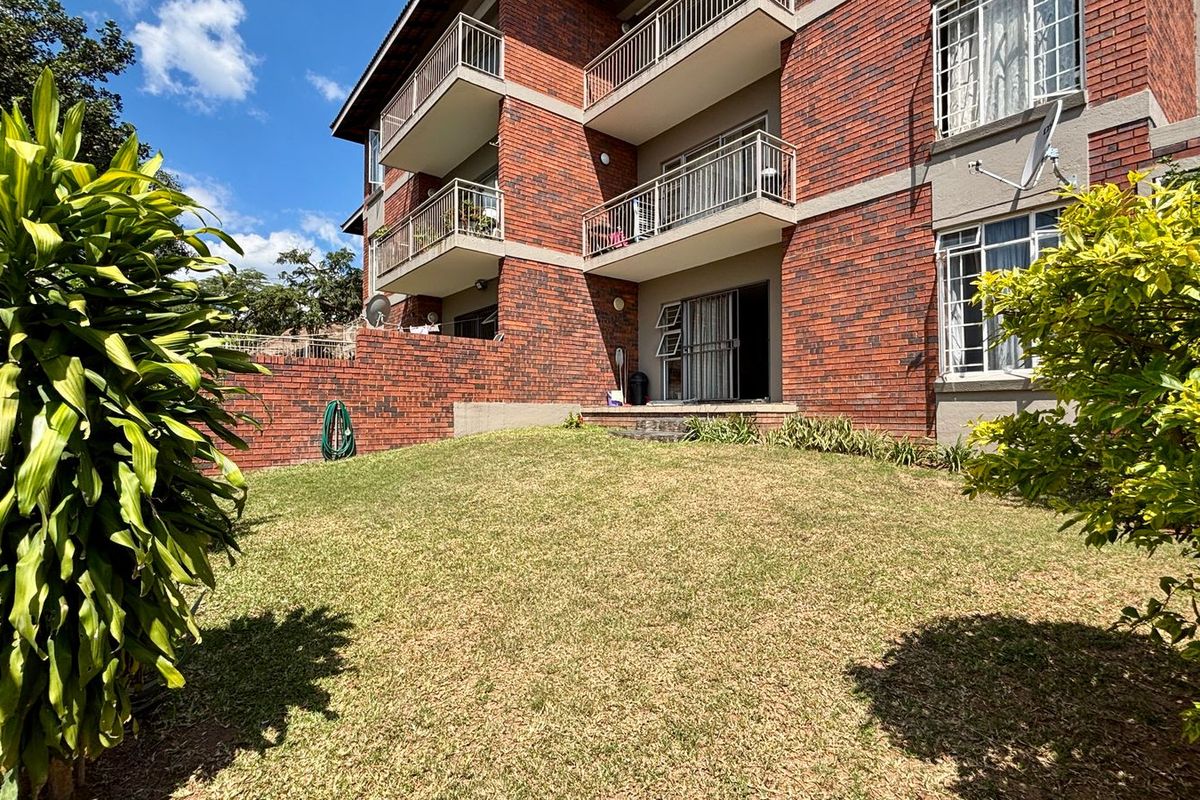 Rear view of a multi-story apartment building featuring face brick construction, private balconies with metal railings, and a well-maintained lawn area.