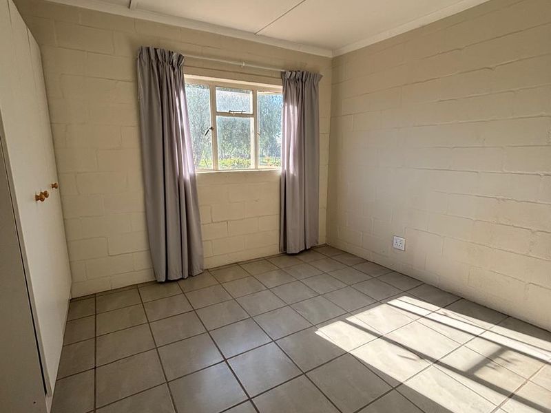 A simple, empty bedroom featuring tiled flooring, exposed blockwork walls, and a built-in wardrobe, offering a clean canvas for personalization.