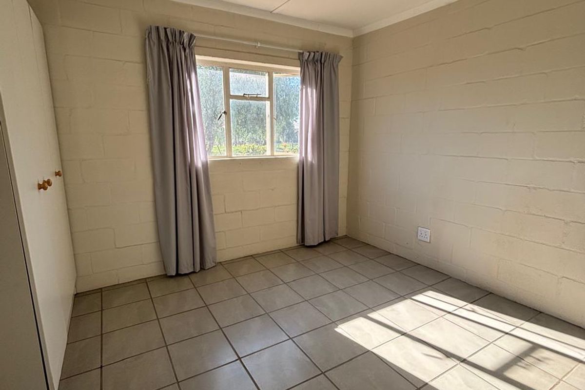 A simple, empty bedroom featuring tiled flooring, exposed blockwork walls, and a built-in wardrobe, offering a clean canvas for personalization.