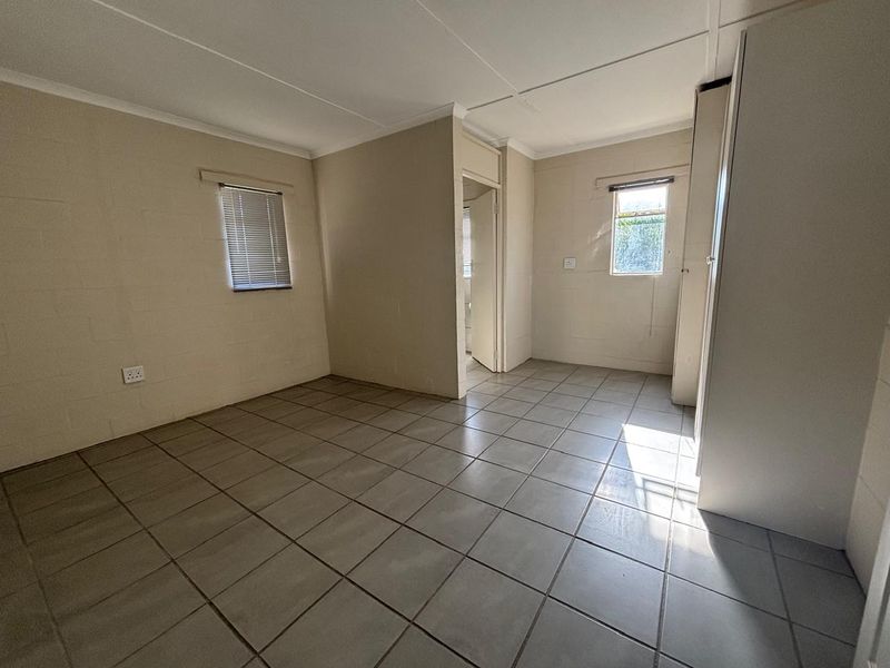 A clean, empty bedroom featuring neutral tiled flooring, built-in storage cupboards, and natural light through windows with fitted venetian blinds.