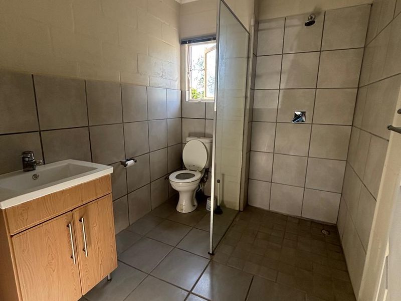 A functional bathroom featuring a vanity cabinet, toilet, and a walk-in shower with a glass screen and tiled finishes.