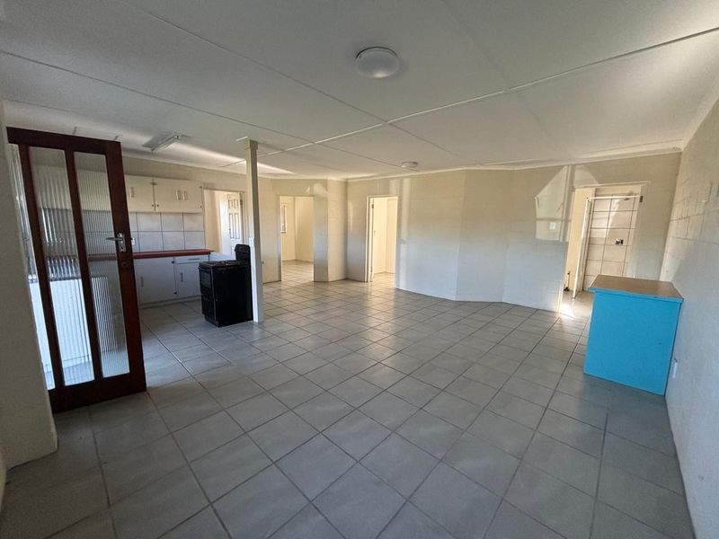 Spacious open-plan living and kitchen area featuring tiled flooring, built-in cabinetry, and multiple access points to other rooms in the house.