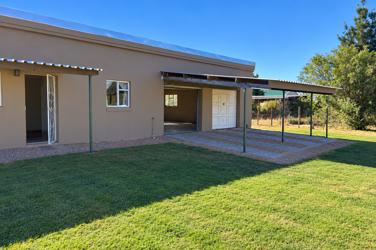 Rear view of the property featuring a covered patio area, paved driveway, and garage access, set against a well-maintained lawn.