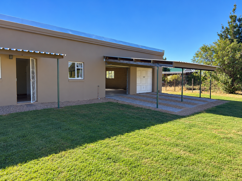 Rear view of the property featuring a covered patio area, paved driveway, and garage access, set against a well-maintained lawn.