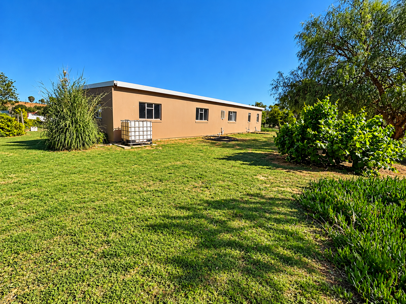 A view of the rear exterior of the house, featuring a large lawn, established garden, and a water storage tank.