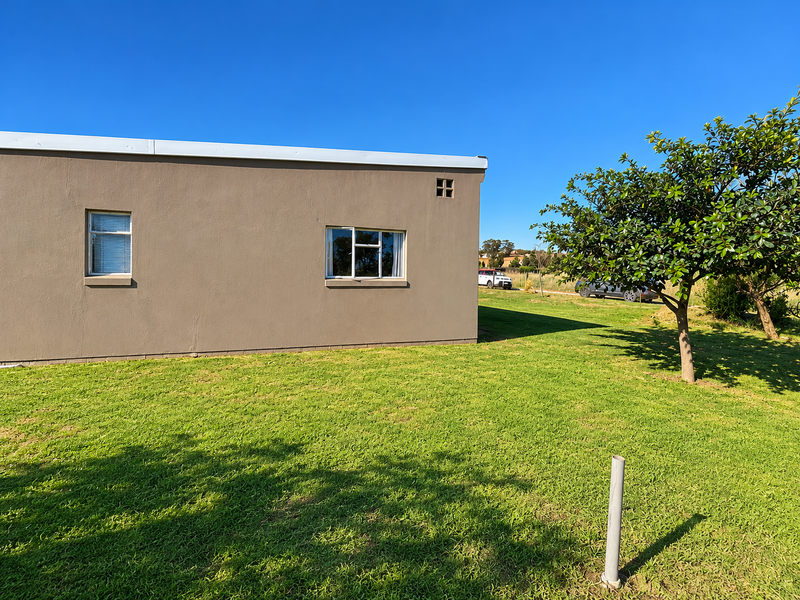 A view of the rear exterior wall of the house featuring plastered finishes, aluminium windows, and a well-maintained lawn area.