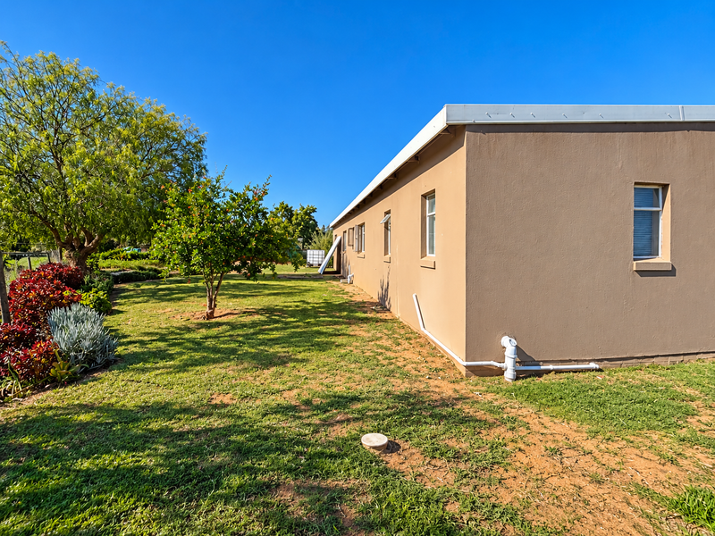 A view of the rear exterior of the house featuring plastered walls, casement windows, and a spacious garden area.