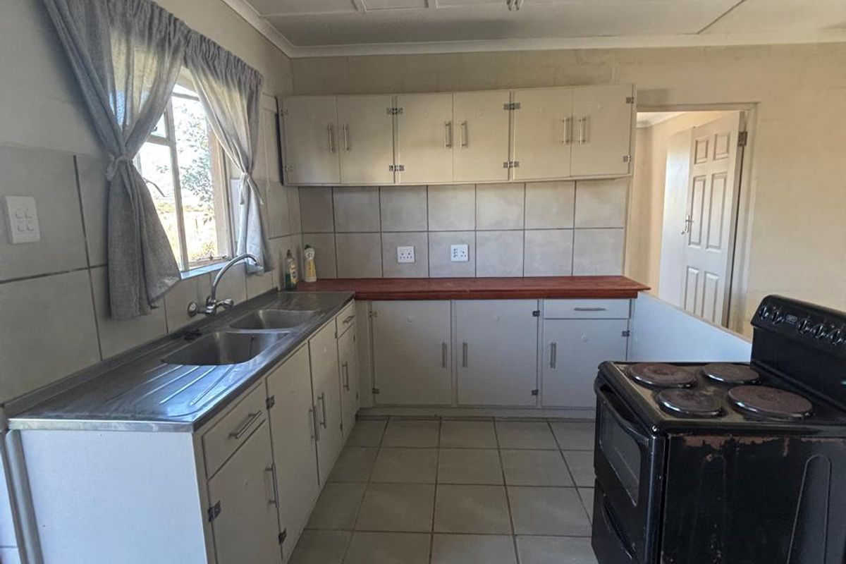 A functional kitchen featuring tiled flooring, built-in cabinetry, a double basin sink, and a tiled backsplash, offering potential for modernization.