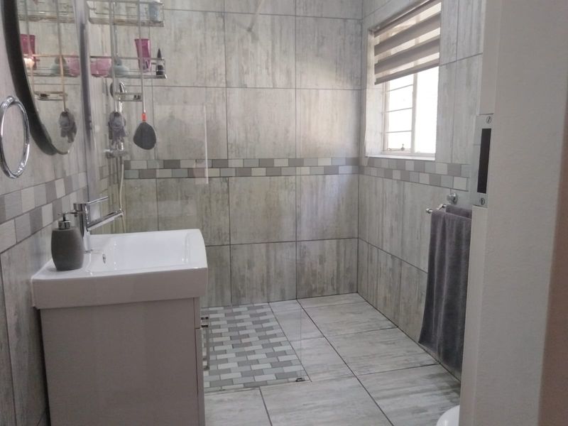 A modern bathroom featuring a vanity cabinet with basin, walk-in shower, and neutral grey tiled finishes throughout.