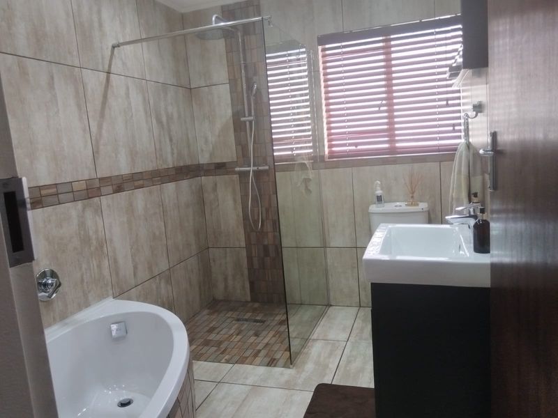 Modern bathroom featuring a walk-in shower with glass screen, a freestanding bathtub, and a vanity basin with tiled finishes throughout.