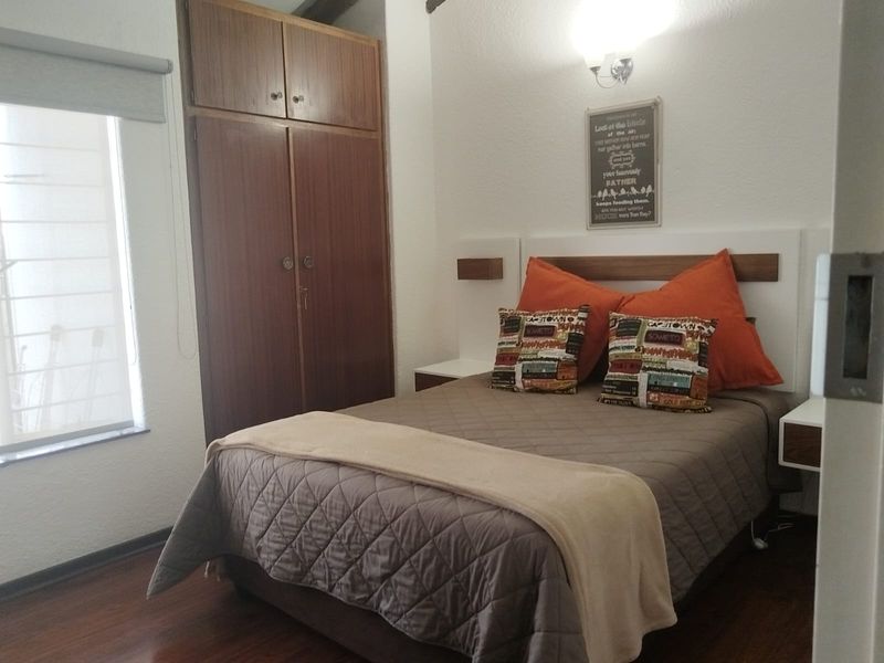 A cozy bedroom featuring laminate flooring, a built-in wooden wardrobe, and wall-mounted bedside tables with integrated lighting.