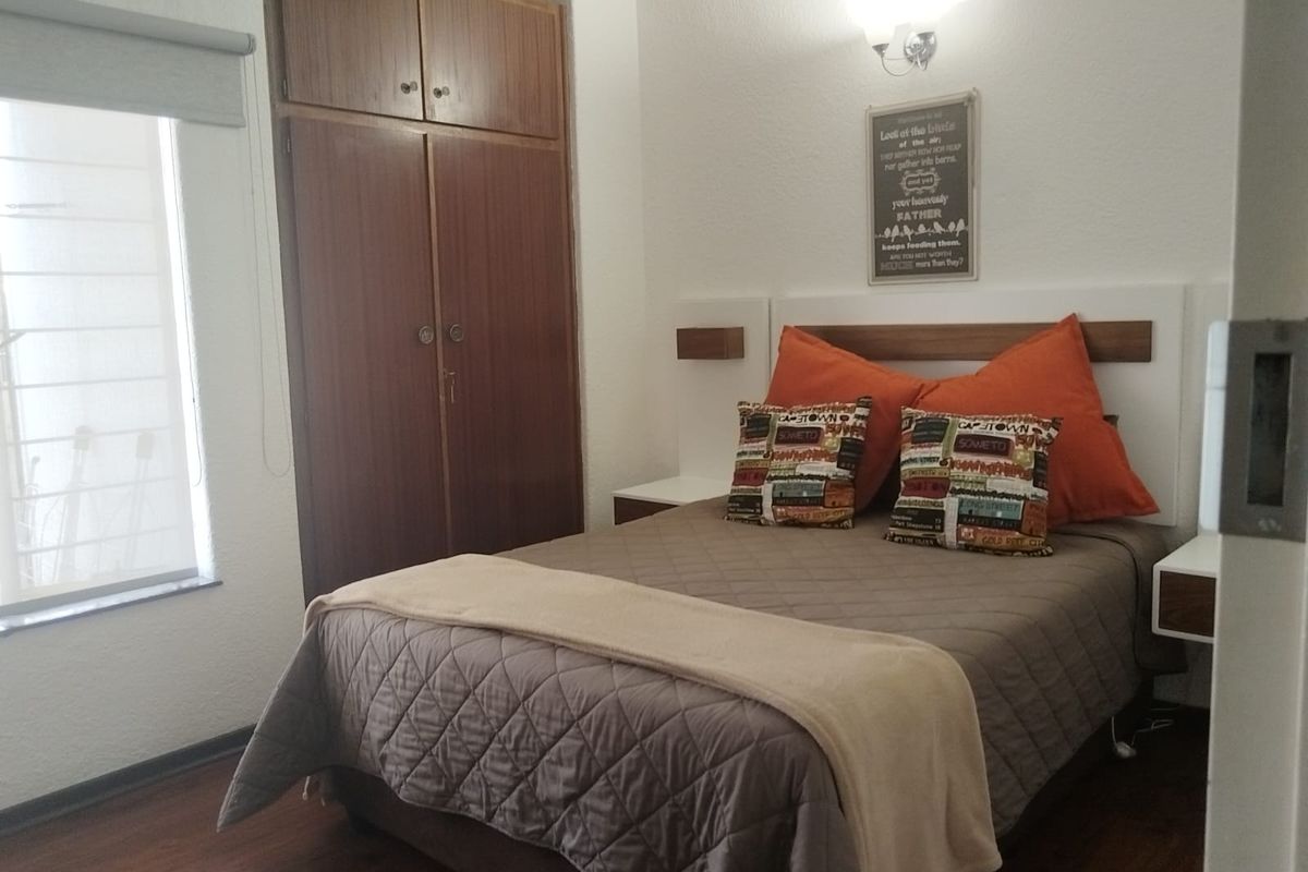 A cozy bedroom featuring laminate flooring, a built-in wooden wardrobe, and wall-mounted bedside tables with integrated lighting.