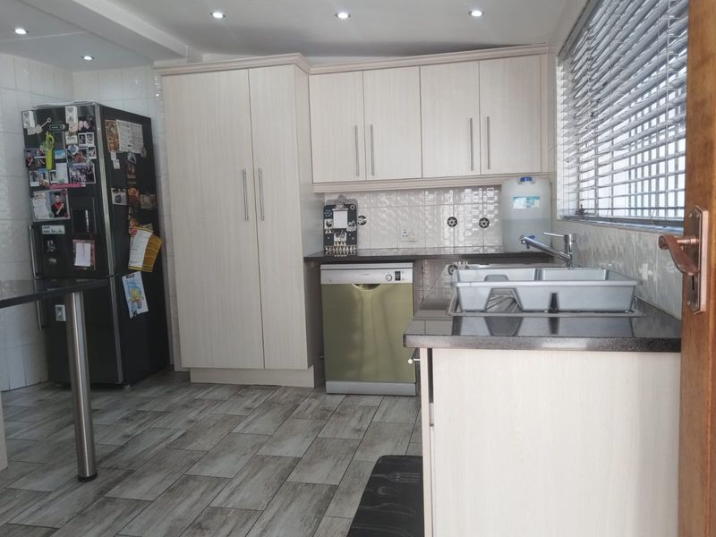 A functional kitchen featuring light wood-grain cabinetry, dark granite countertops, a double sink, and integrated dishwasher, complemented by tiled flooring and recessed lighting.