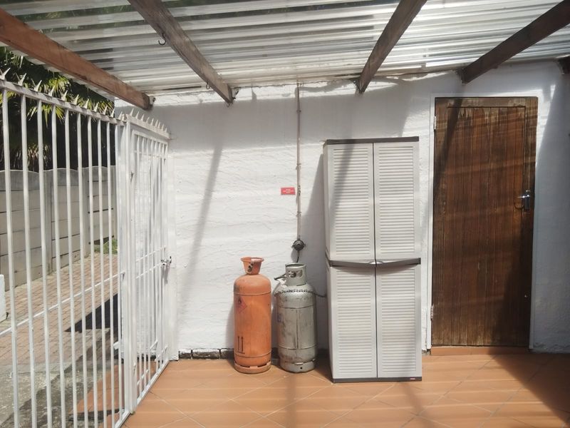 A covered outdoor patio area featuring tiled flooring, a corrugated roof structure, and a secure entrance door.