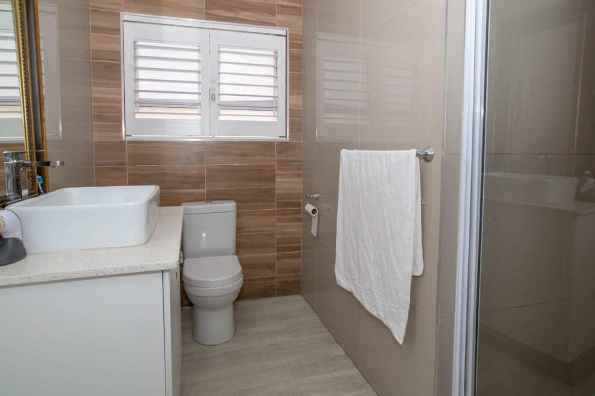 A modern bathroom featuring a vessel sink, vanity cabinet, toilet, and a glass-enclosed shower with neutral-toned wall and floor tiles.