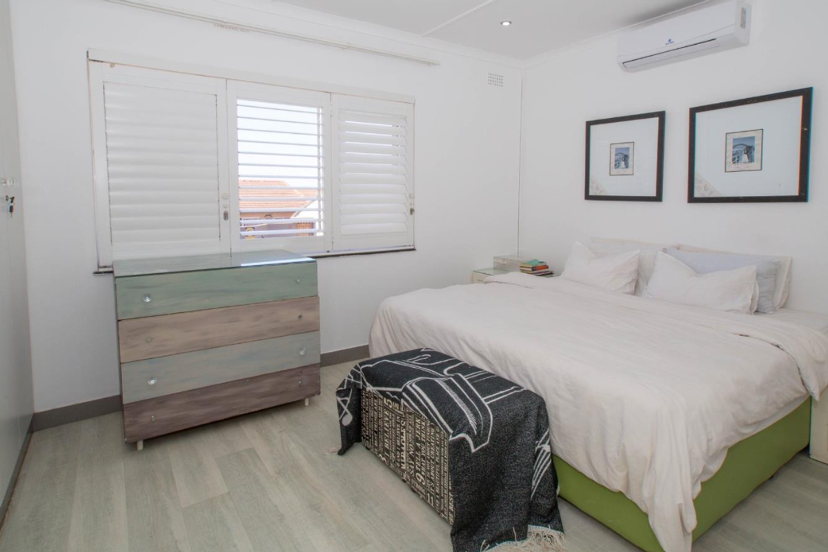 A well-maintained bedroom featuring laminate flooring, plantation shutters, built-in cupboards, and a wall-mounted split-system air conditioner.