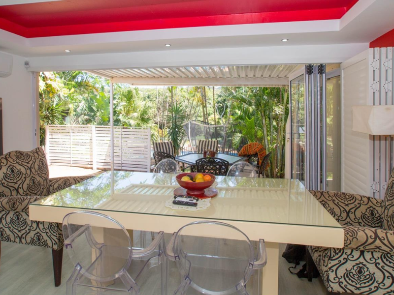 Open plan living area featuring recessed ceiling lighting, split-system air conditioning, and bi-fold glass doors opening onto a lush outdoor patio space.