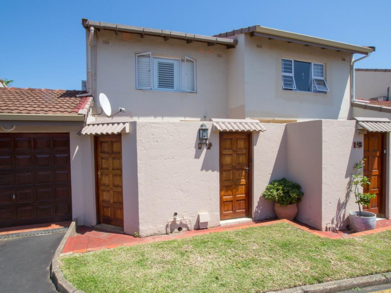 Front elevation of a townhouse featuring a garage, wooden entrance doors, tiled roof, and a small front garden area.
