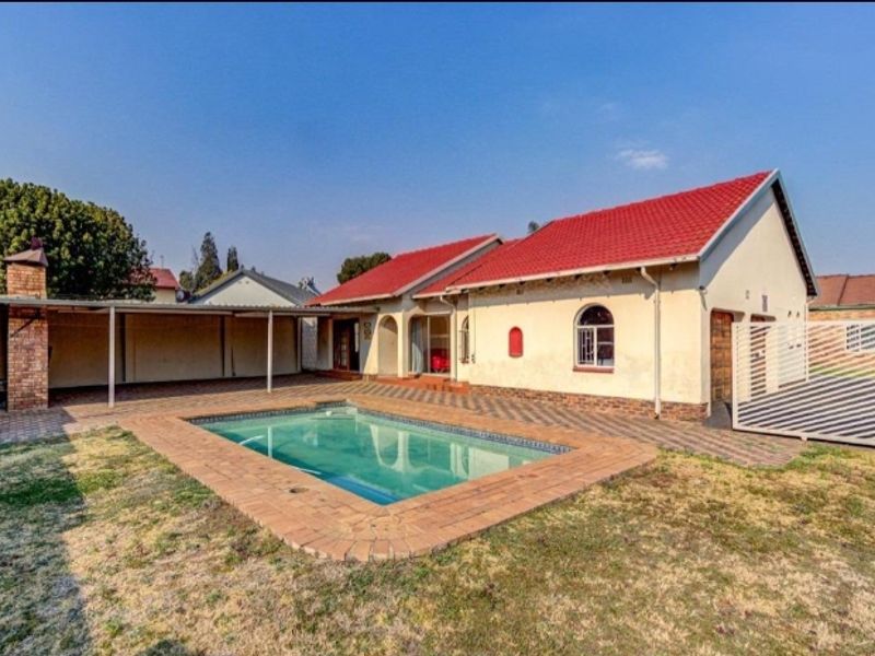 Rear exterior view featuring a swimming pool, paved patio area, covered outdoor space, and a well-maintained tiled roof structure.
