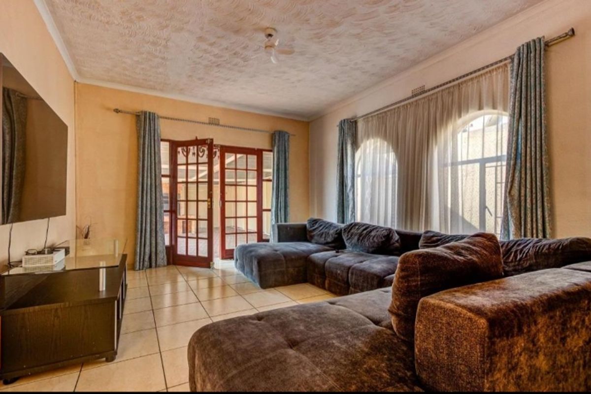 Spacious living room featuring tiled flooring, arched windows, and direct access to the patio through classic french doors.